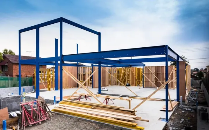 Blue steel frame of a building under construction, wooden studs, concrete foundation.