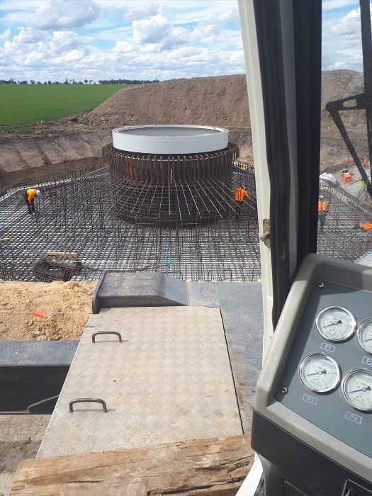 Construction site with rebar and concrete formwork for a large circular structure, viewed from inside a cab.