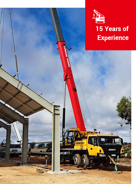 Crane lifting steel beams for a building under construction. Yellow crane, red boom, blue sky, 15 years experience.