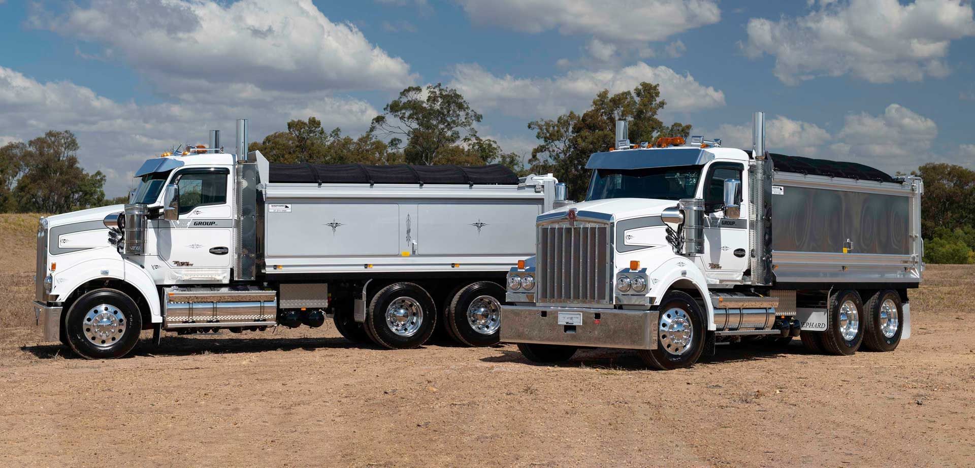 Two dump trucks are parked next to each other in a dirt field.