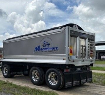 Silver Mitchelimore semi-trailer on a road, under a cloudy sky.