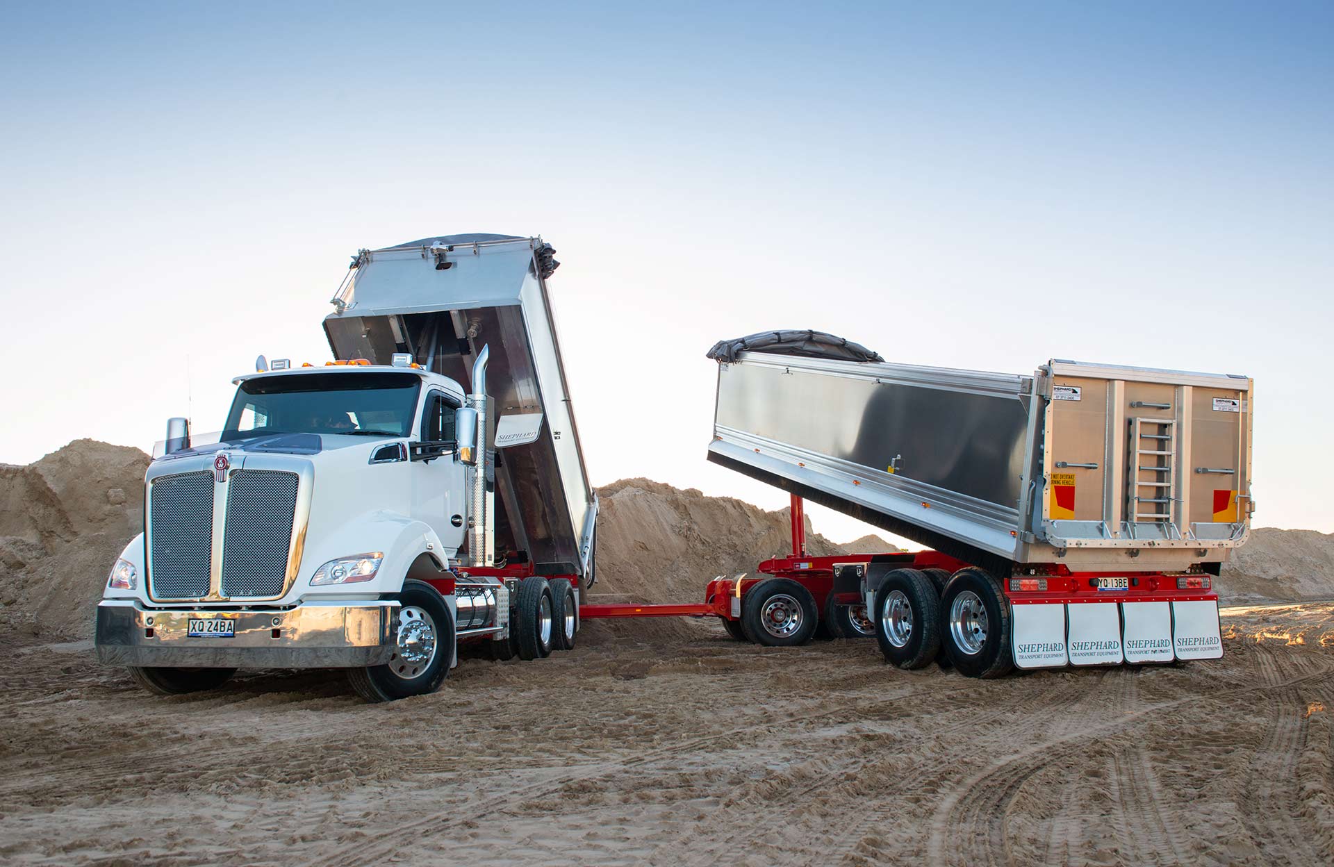 A dump truck with a trailer attached to it is parked in a dirt field.