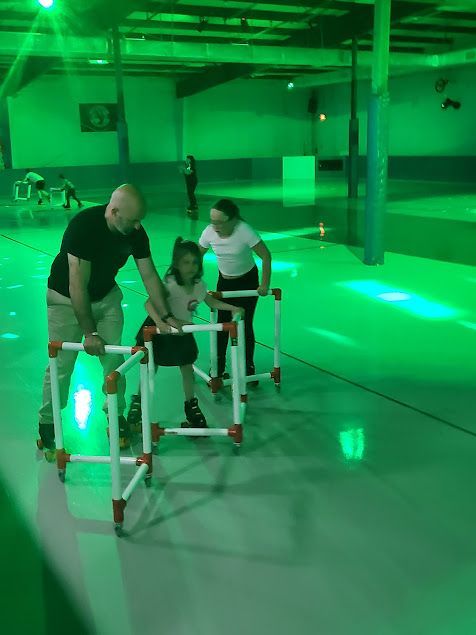 A man is helping a little girl roller skate on a roller rink.