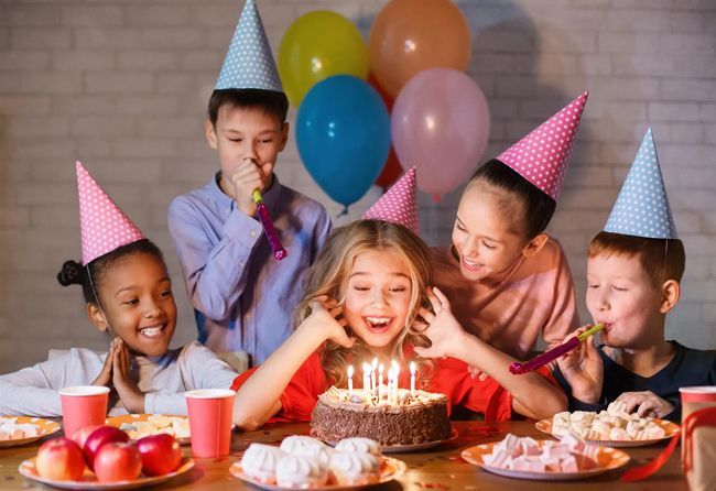 A group of children are celebrating a birthday with a cake and balloons.