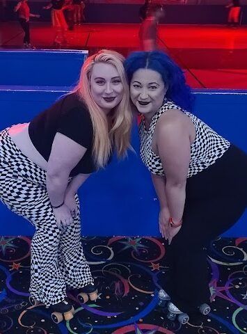 Two women are posing for a picture at a roller rink