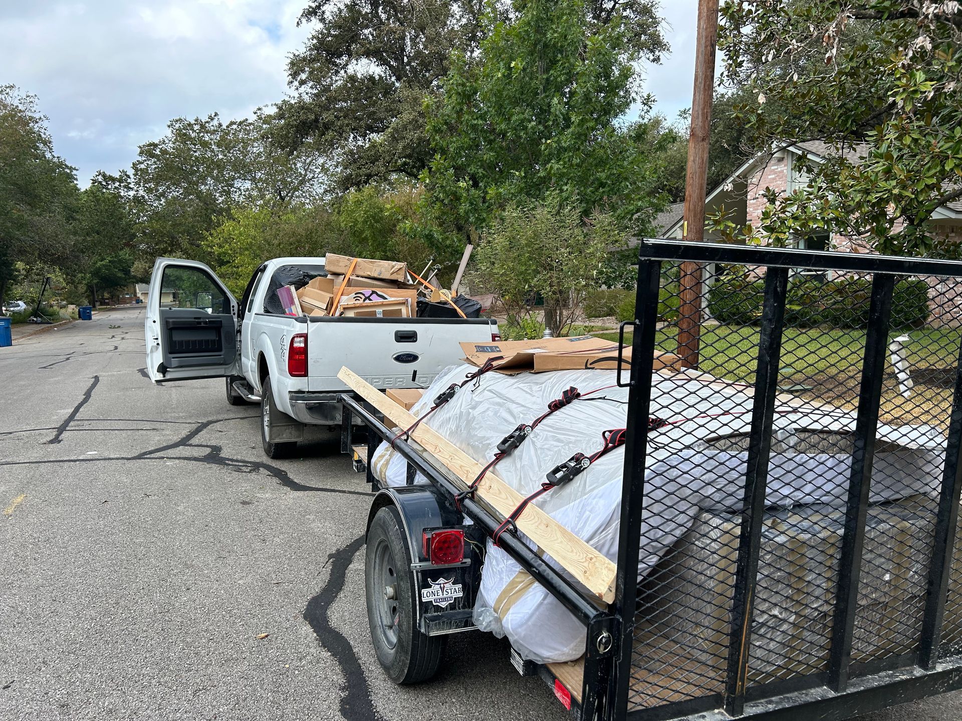 White truck with open door and trailer loaded with materials on a residential street.
