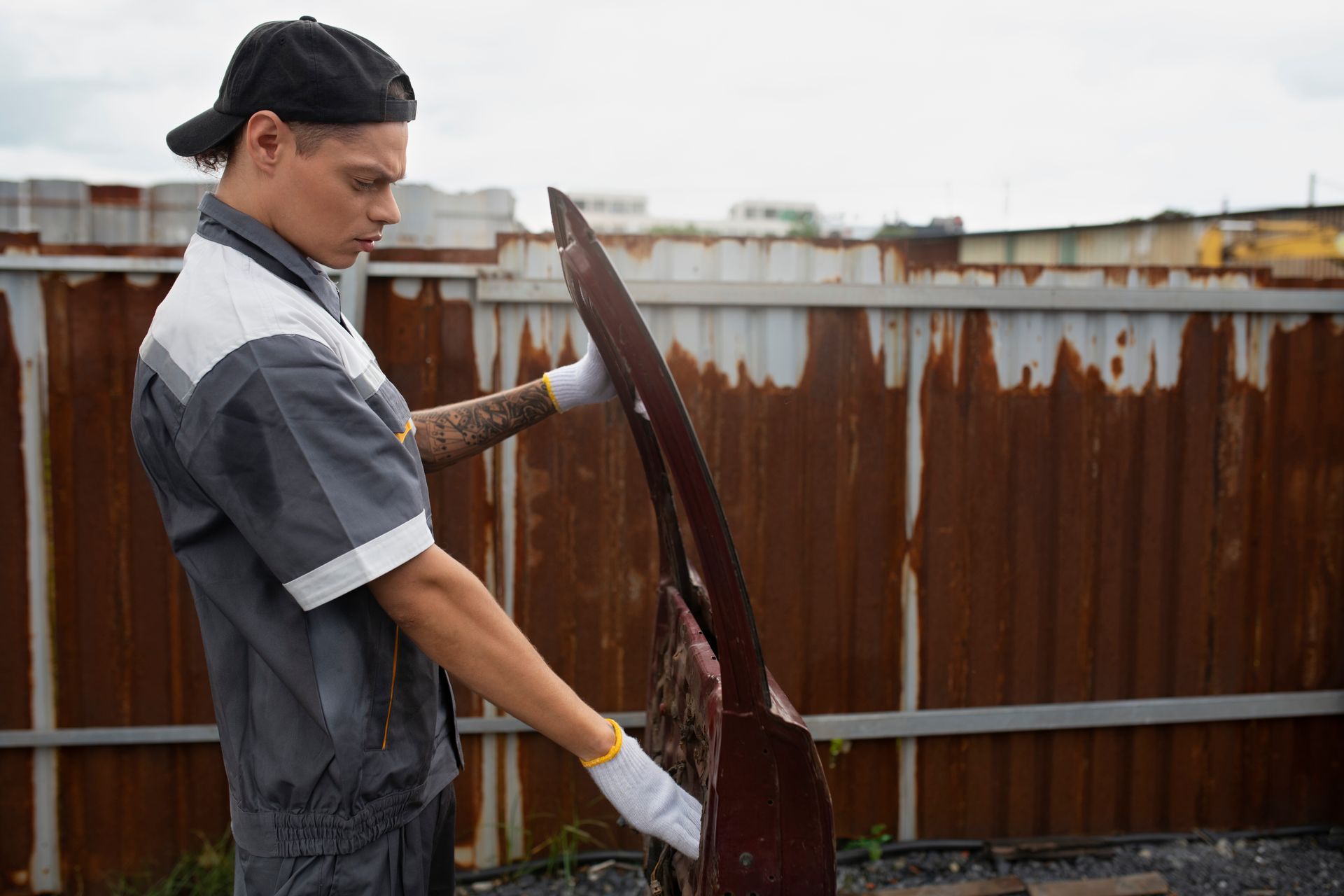 A man is holding a piece of metal in front of a rusty fence.