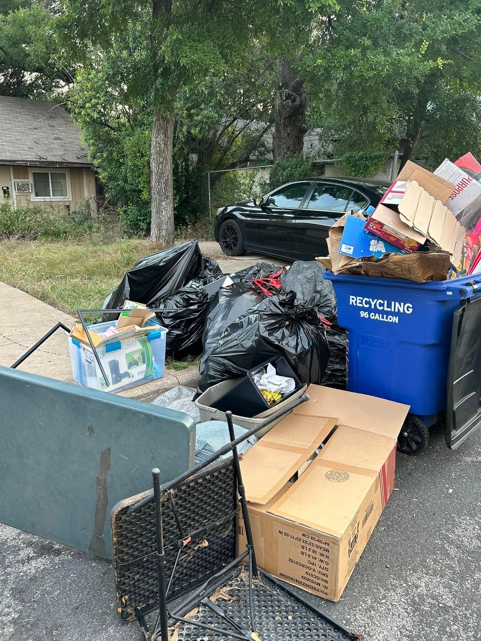 A pile of trash is sitting on the side of the road next to a trash can.