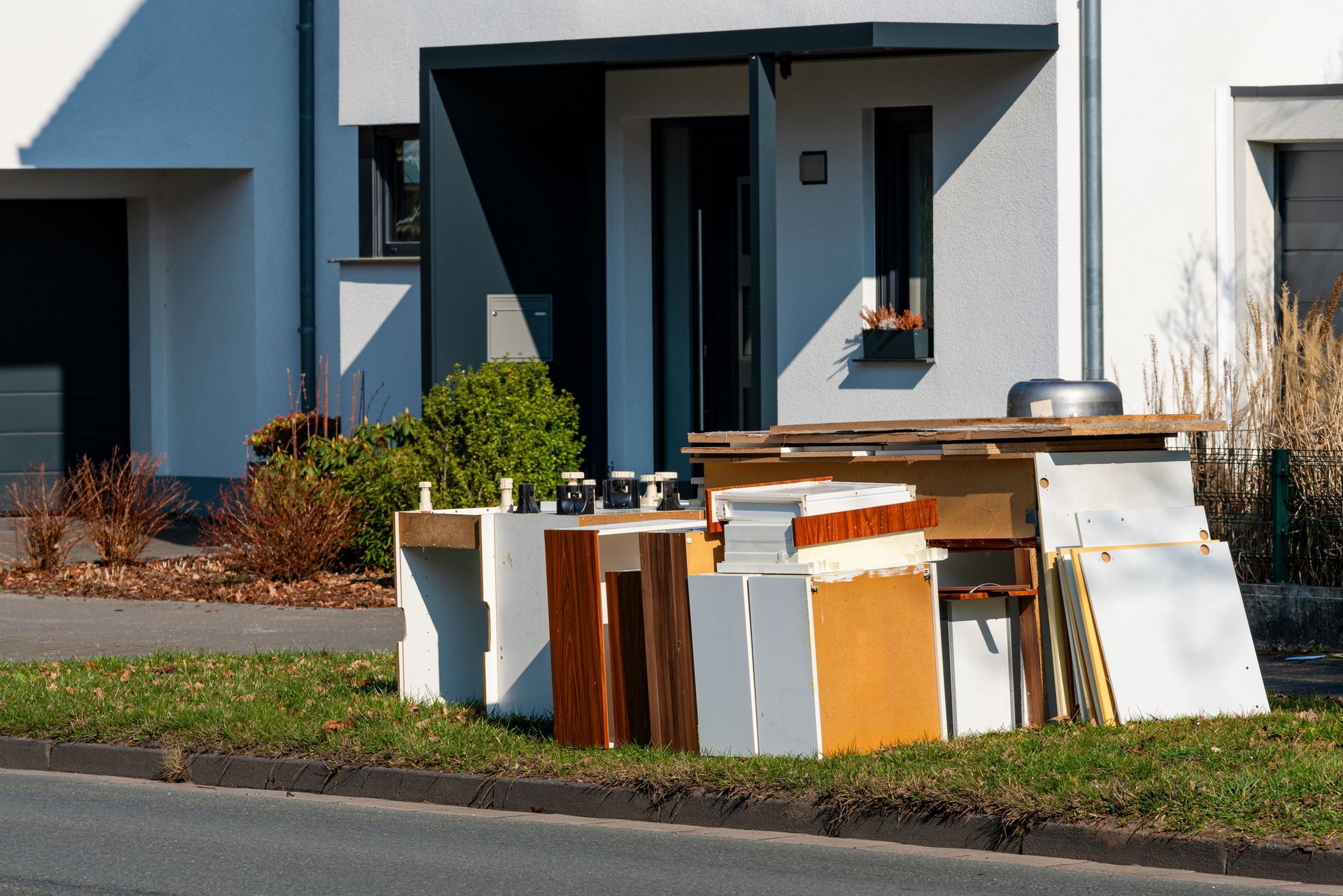 A pile of furniture is sitting on the side of the road in front of a house.
