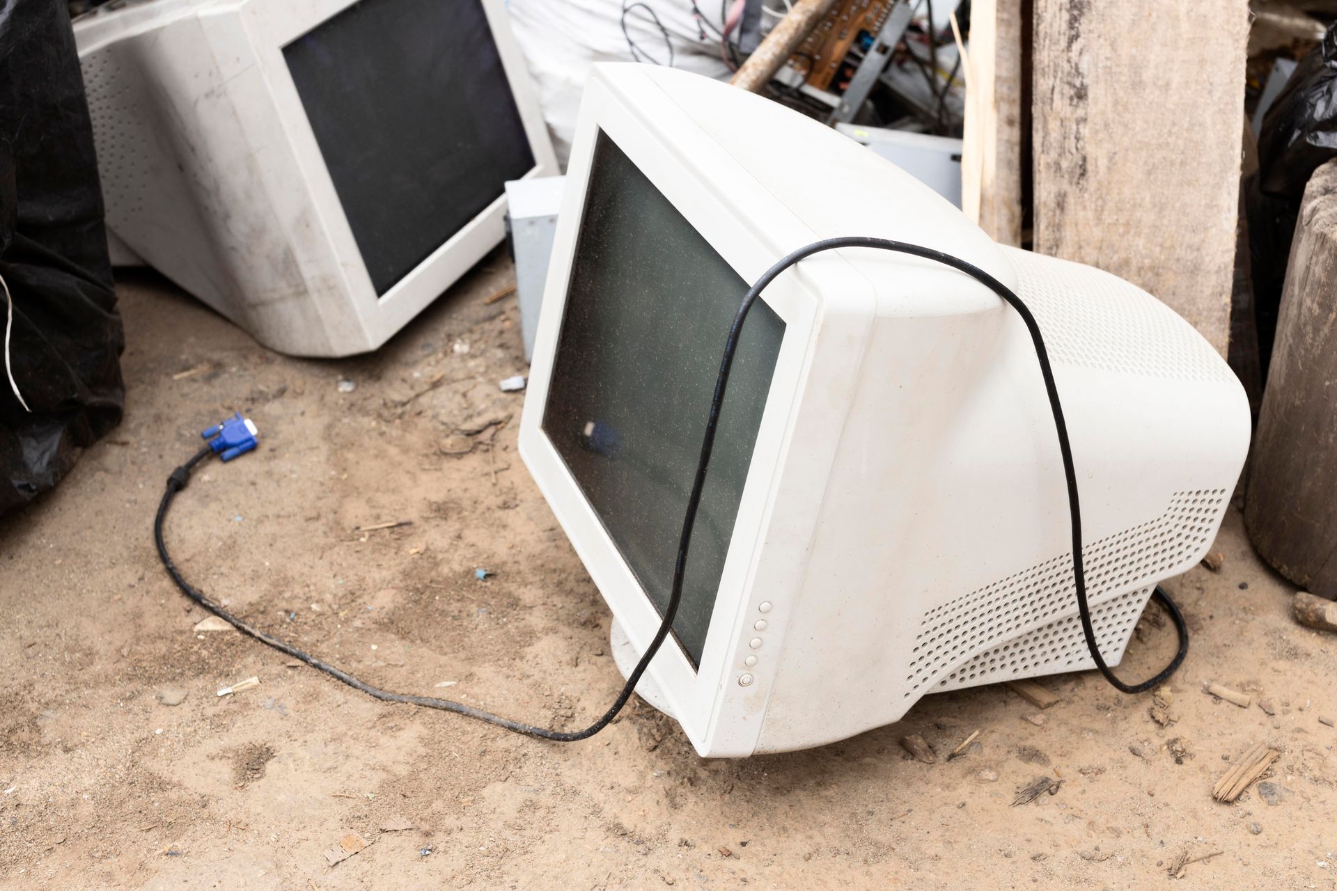 A white computer monitor is sitting on the ground with a cord coming out of it.