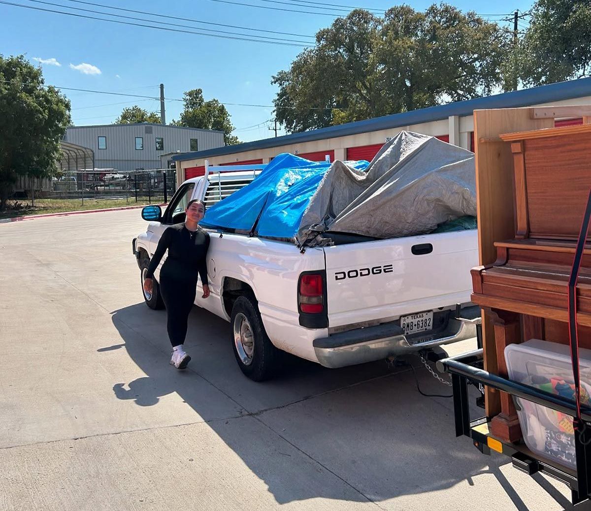 A woman is standing next to a white truck with a blue tarp on the back.
