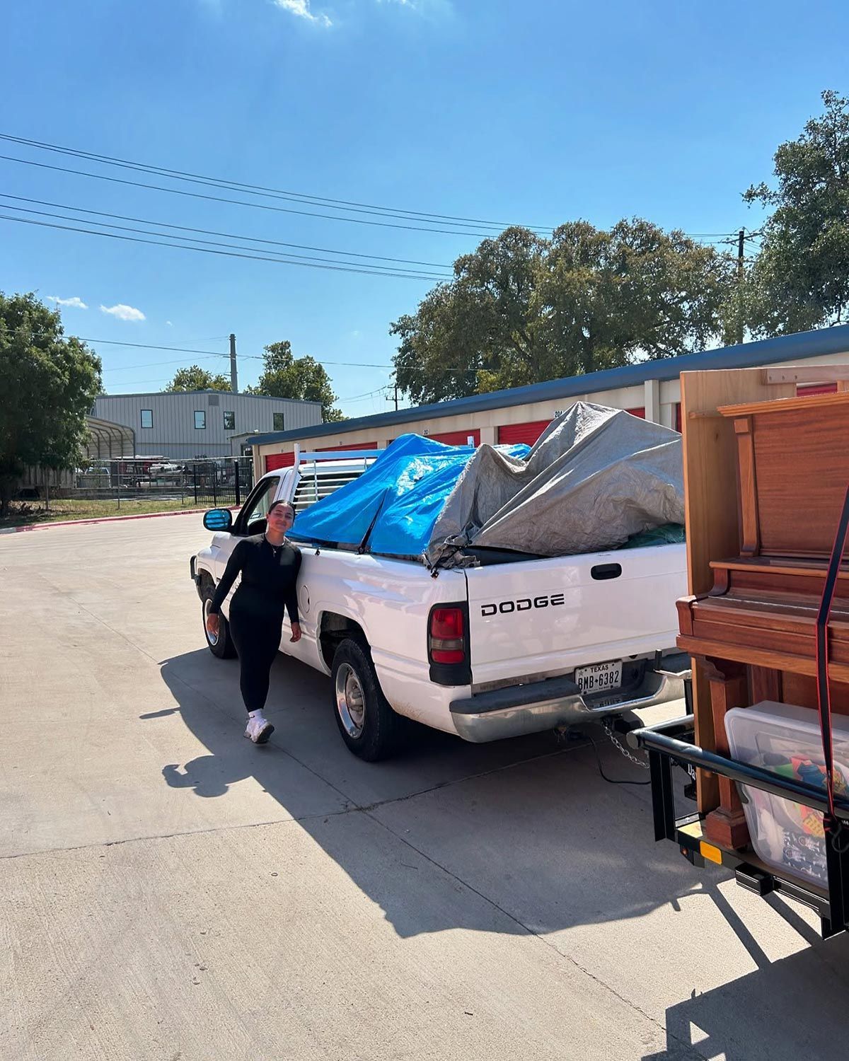 A woman is standing next to a white truck with a blue tarp on the back.