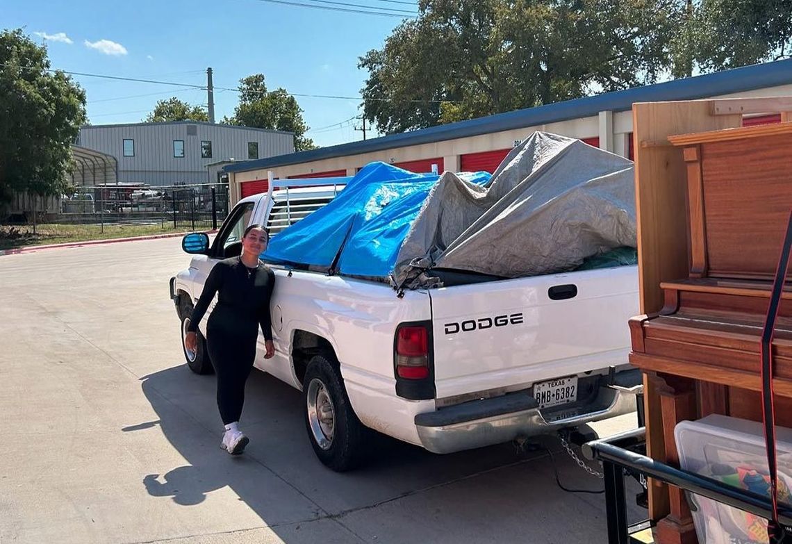 A woman is standing next to a white truck with a blue tarp on the back.
