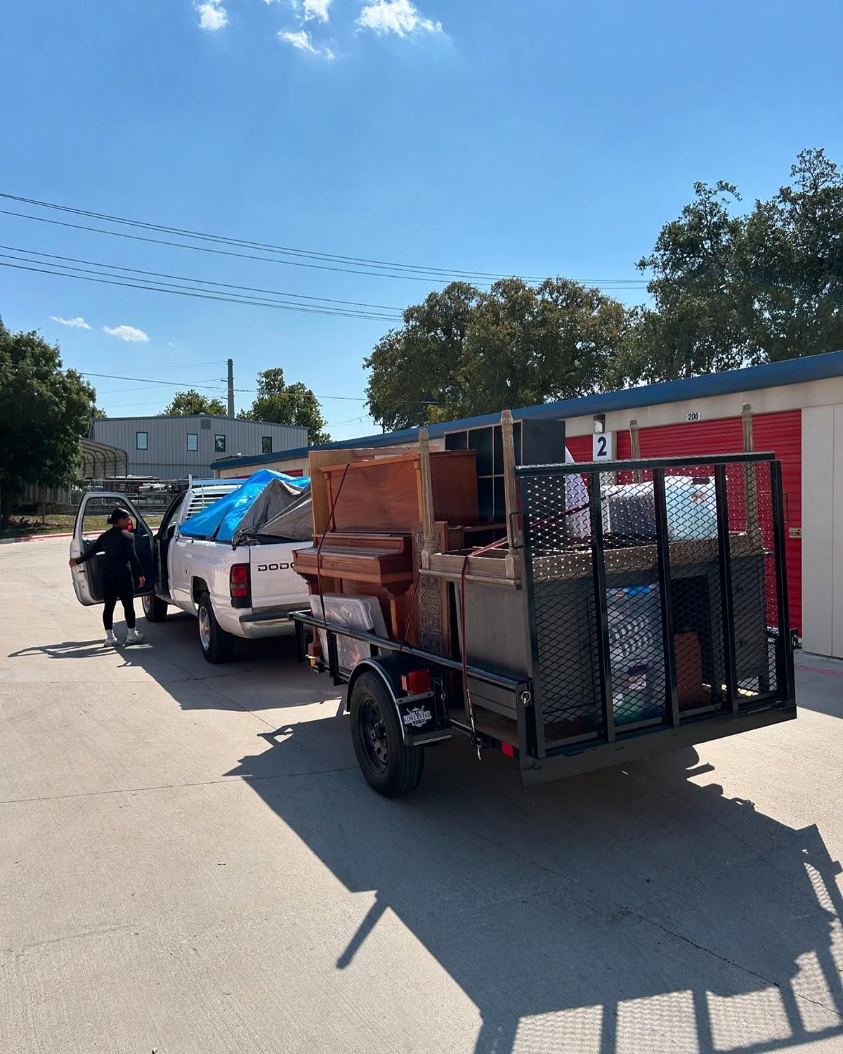 A man is standing next to a truck with a trailer full of junk.