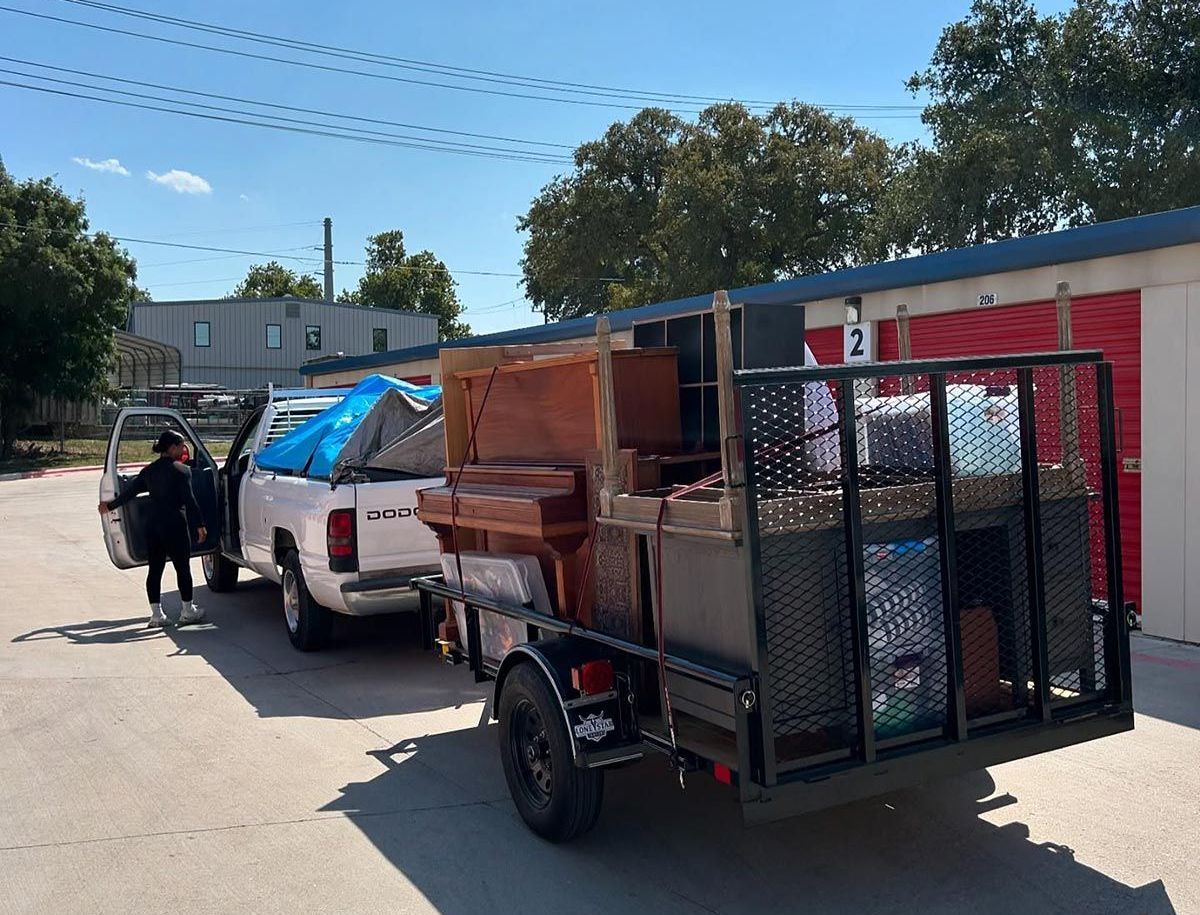 A woman is standing next to a truck with a trailer full of junk.