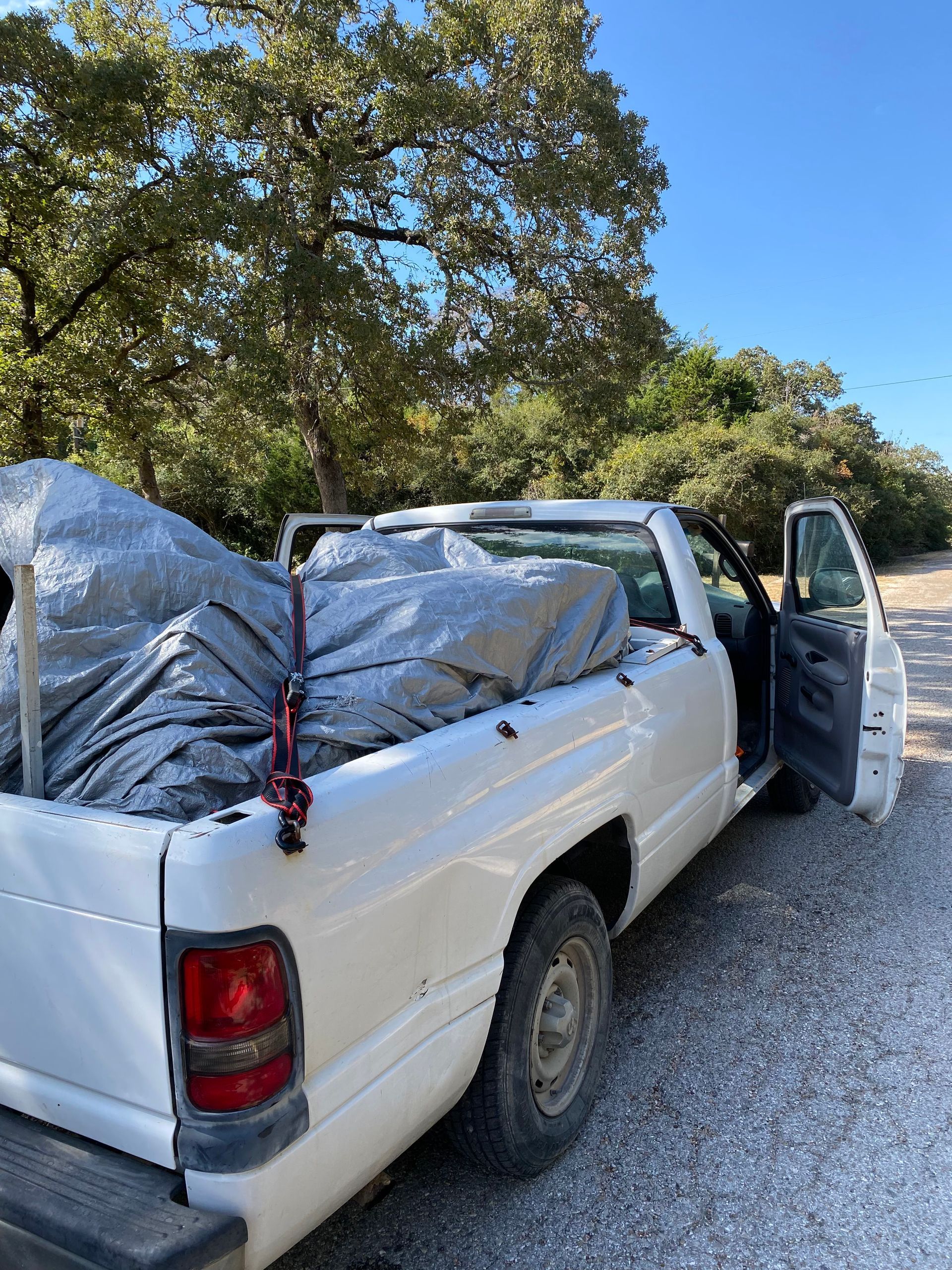 A white truck with a tarp in the bed is parked on a gravel road.