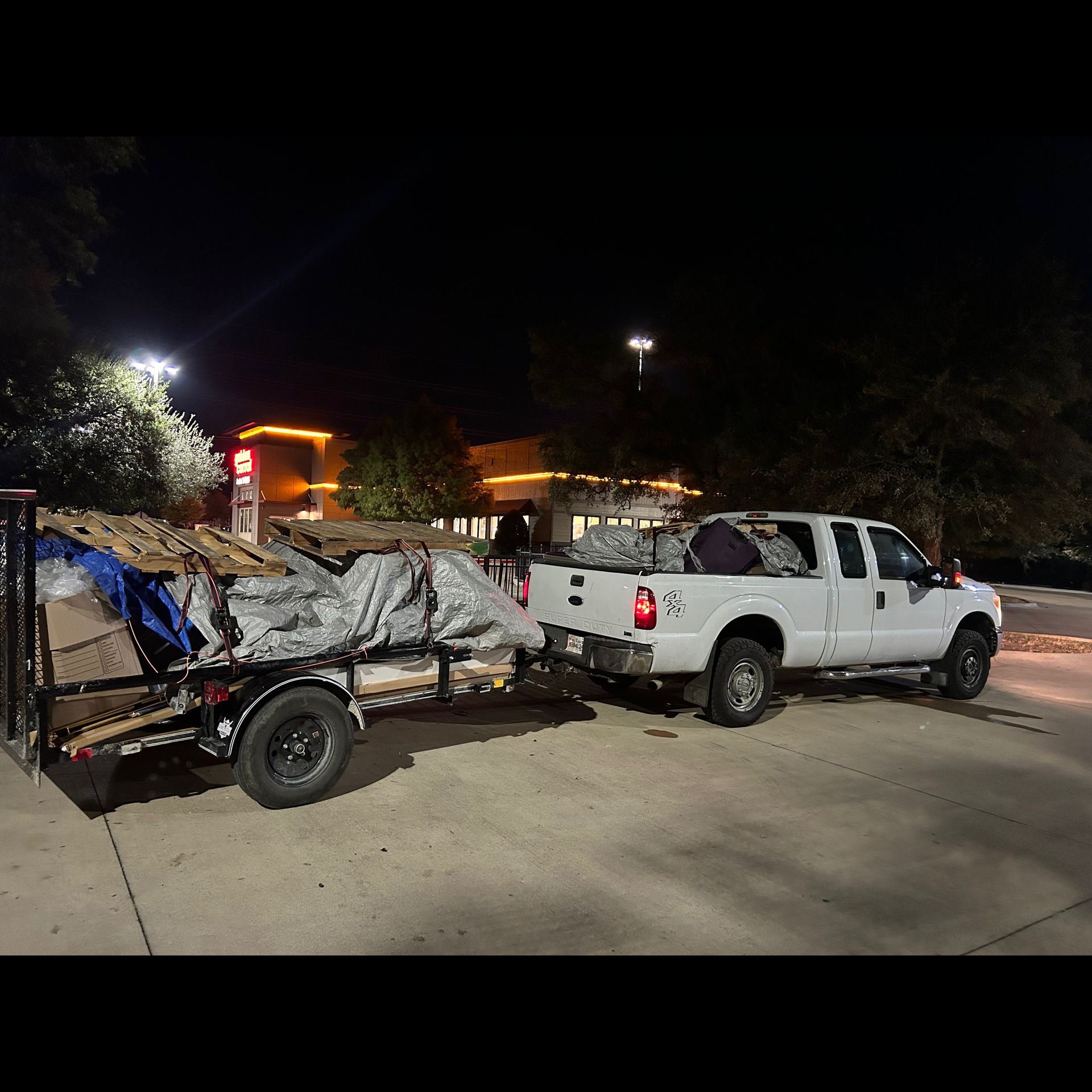 A white truck is pulling a trailer full of junk.