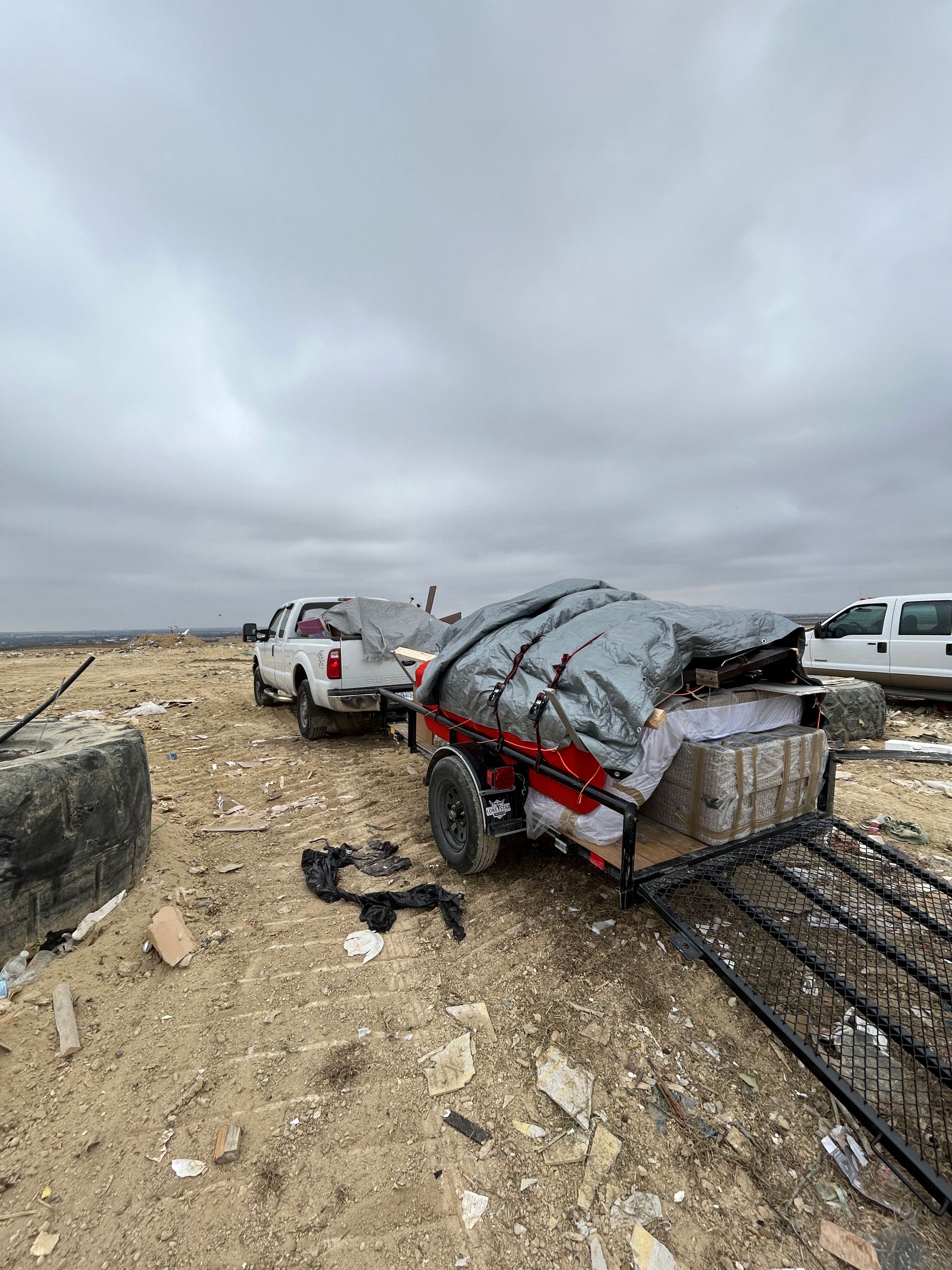 A trailer is sitting in the middle of a dirt field next to a truck.