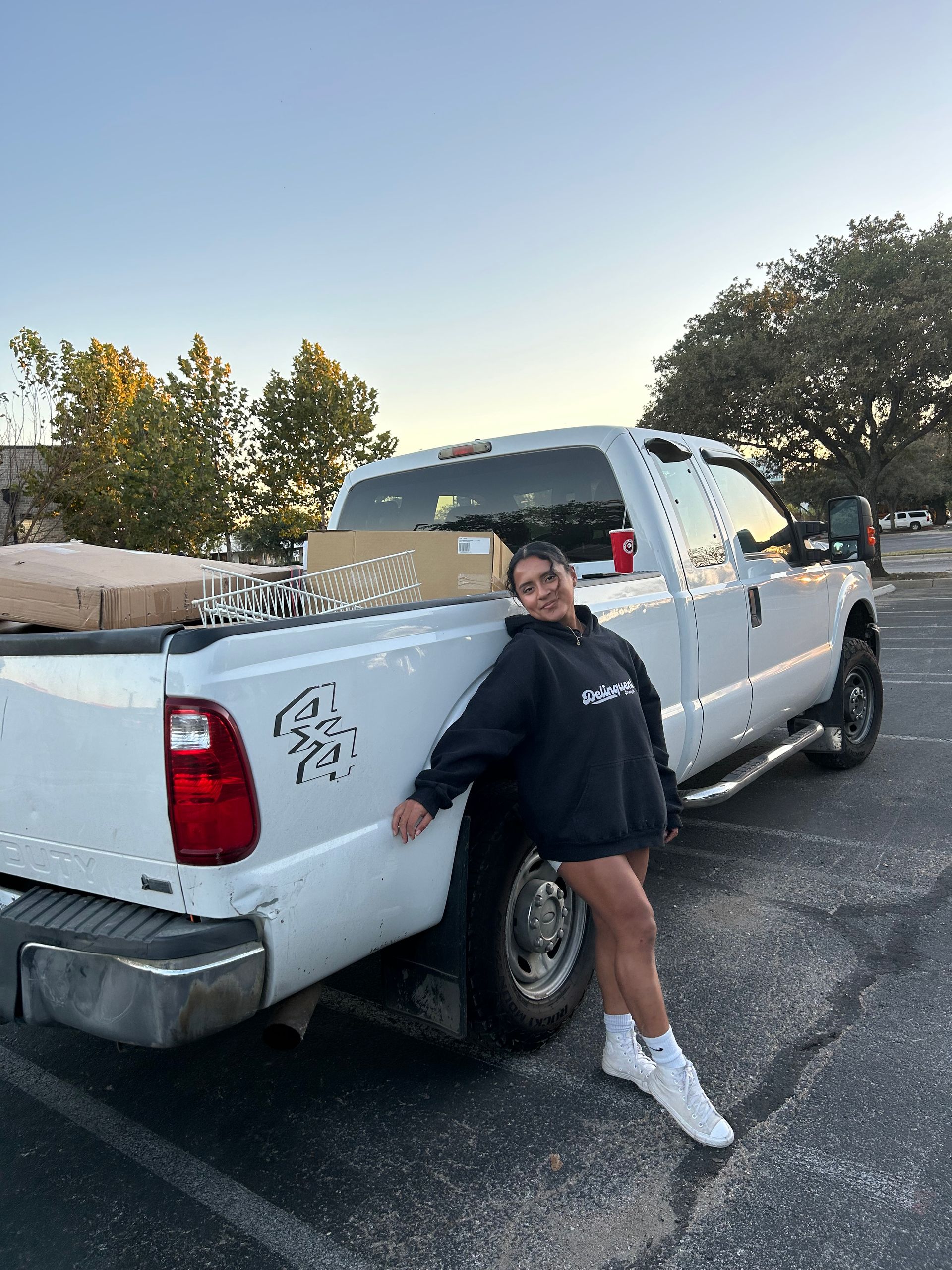 Woman in black hoodie leans against white pickup truck.