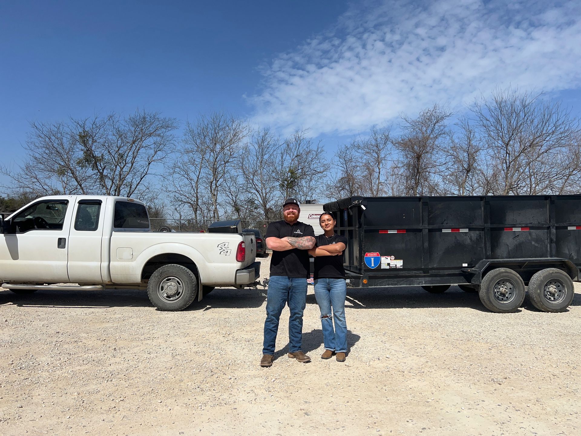 A man and a woman are standing in front of a dump truck and trailer.