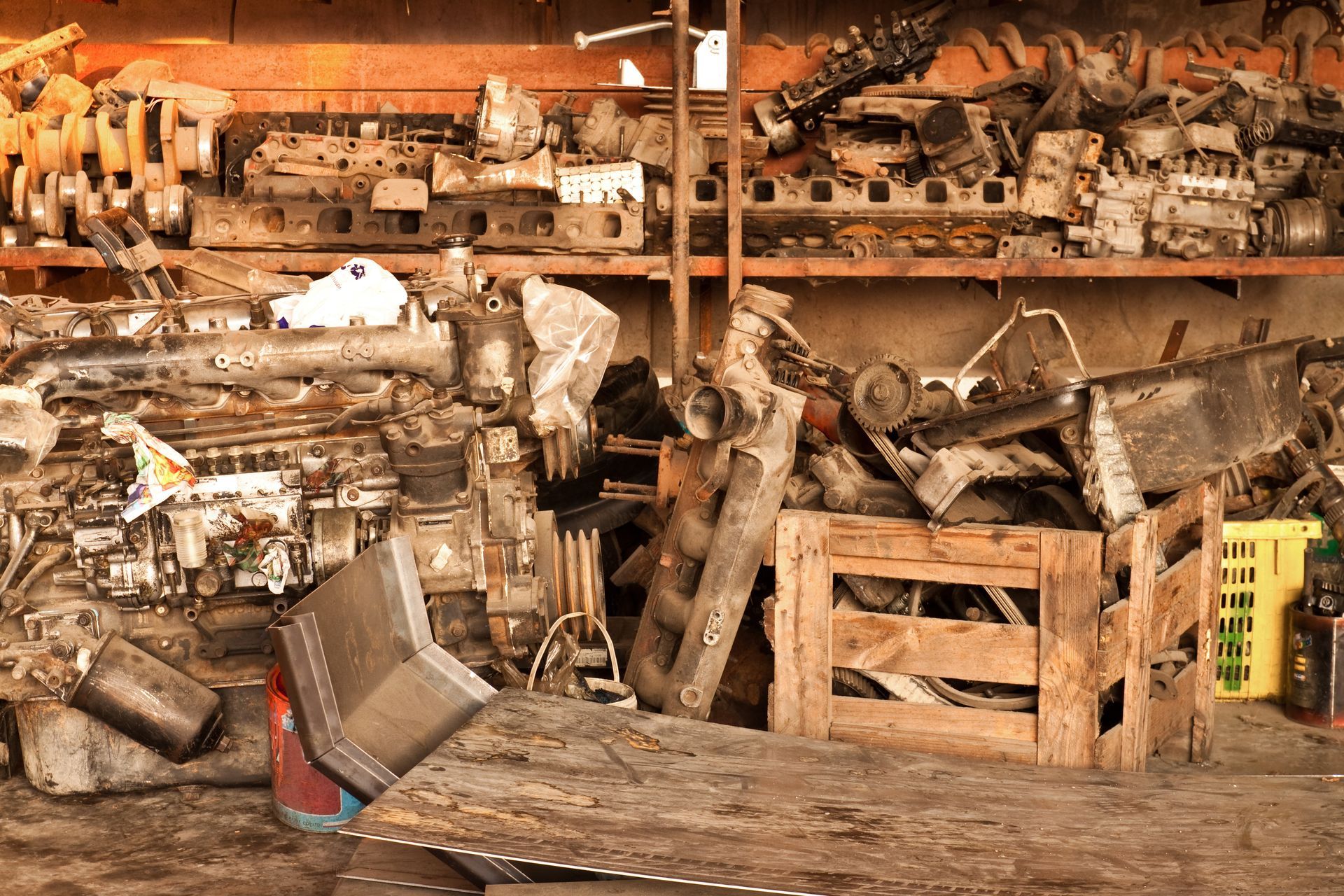 Jumbled pile of automotive parts and engines in a workshop, some on shelves, others in a wooden crate.