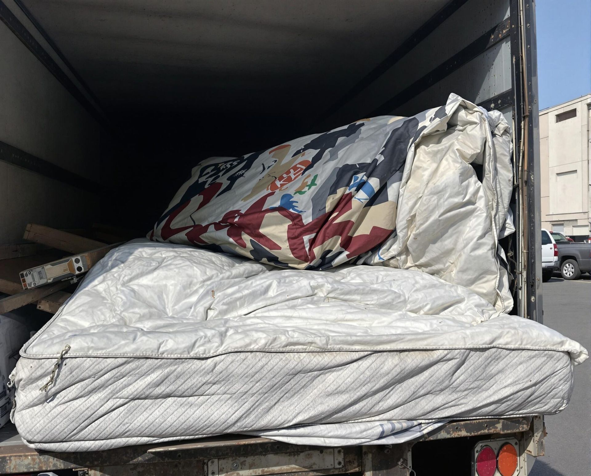 Mattress and a rolled-up patterned item inside the back of a truck.
