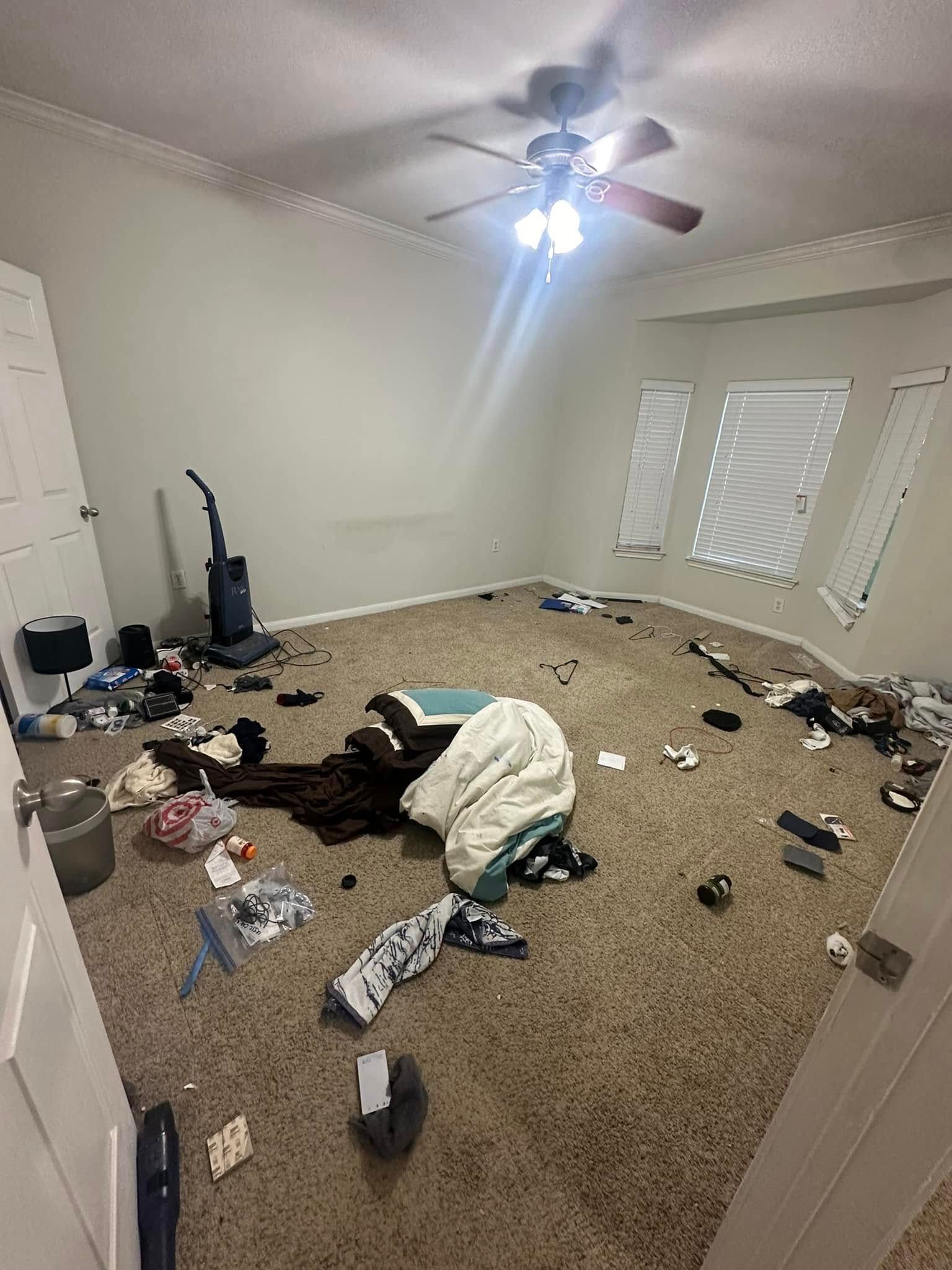 A messy room with a ceiling fan and a vacuum cleaner.