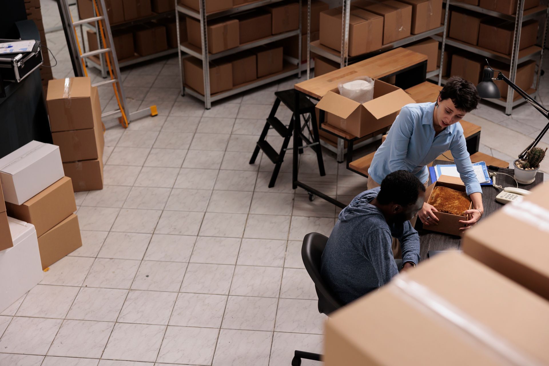 A man and a woman are working in a warehouse filled with boxes.