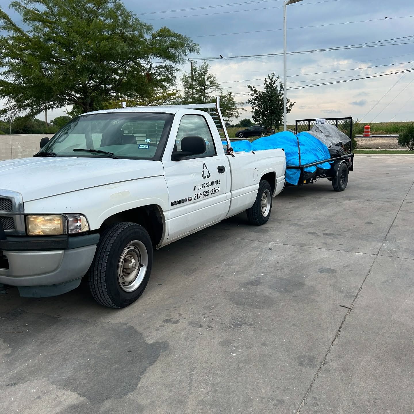 A white truck with a blue tarp on the back is parked in a parking lot.