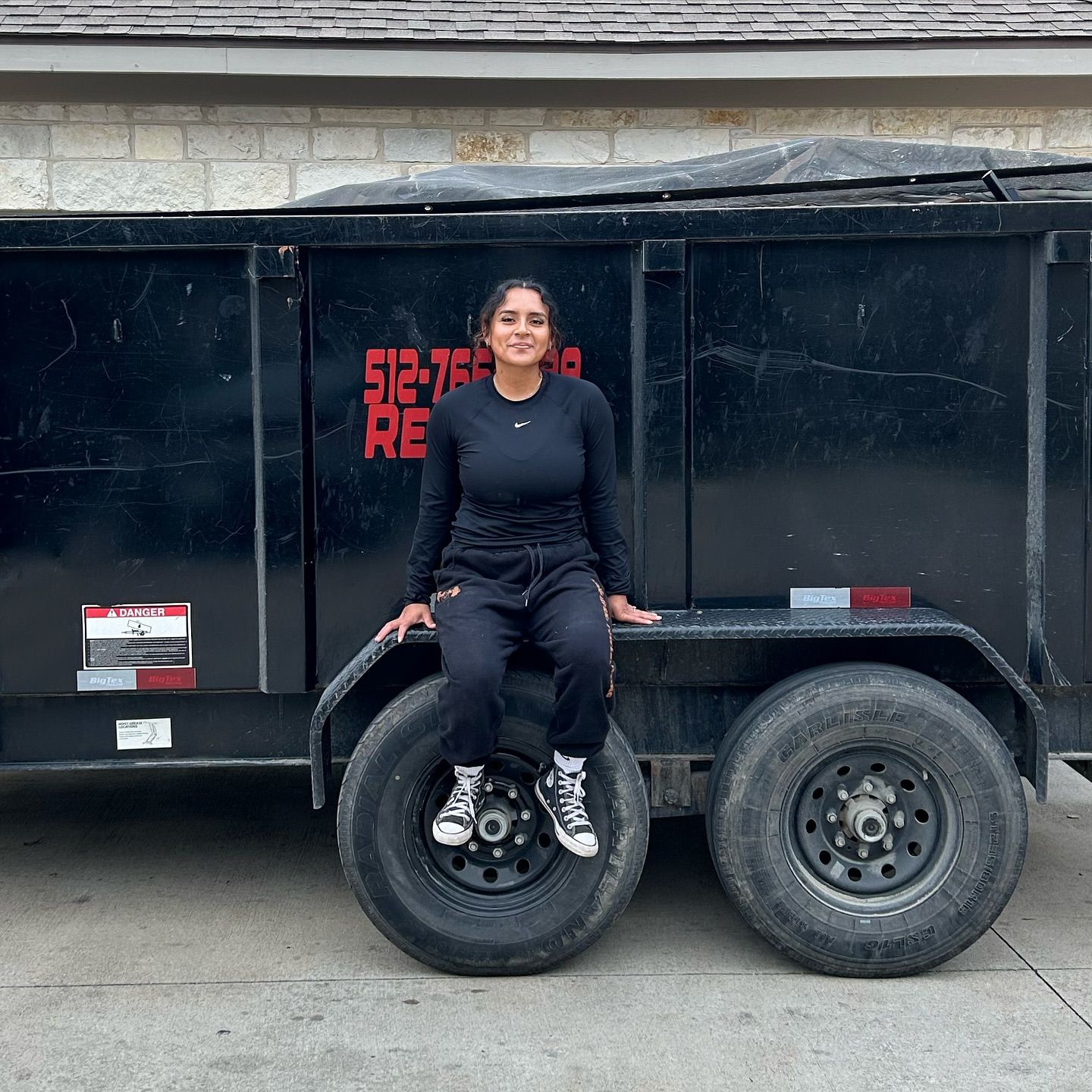 A woman is sitting on the back of a dumpster that says 512-75 re