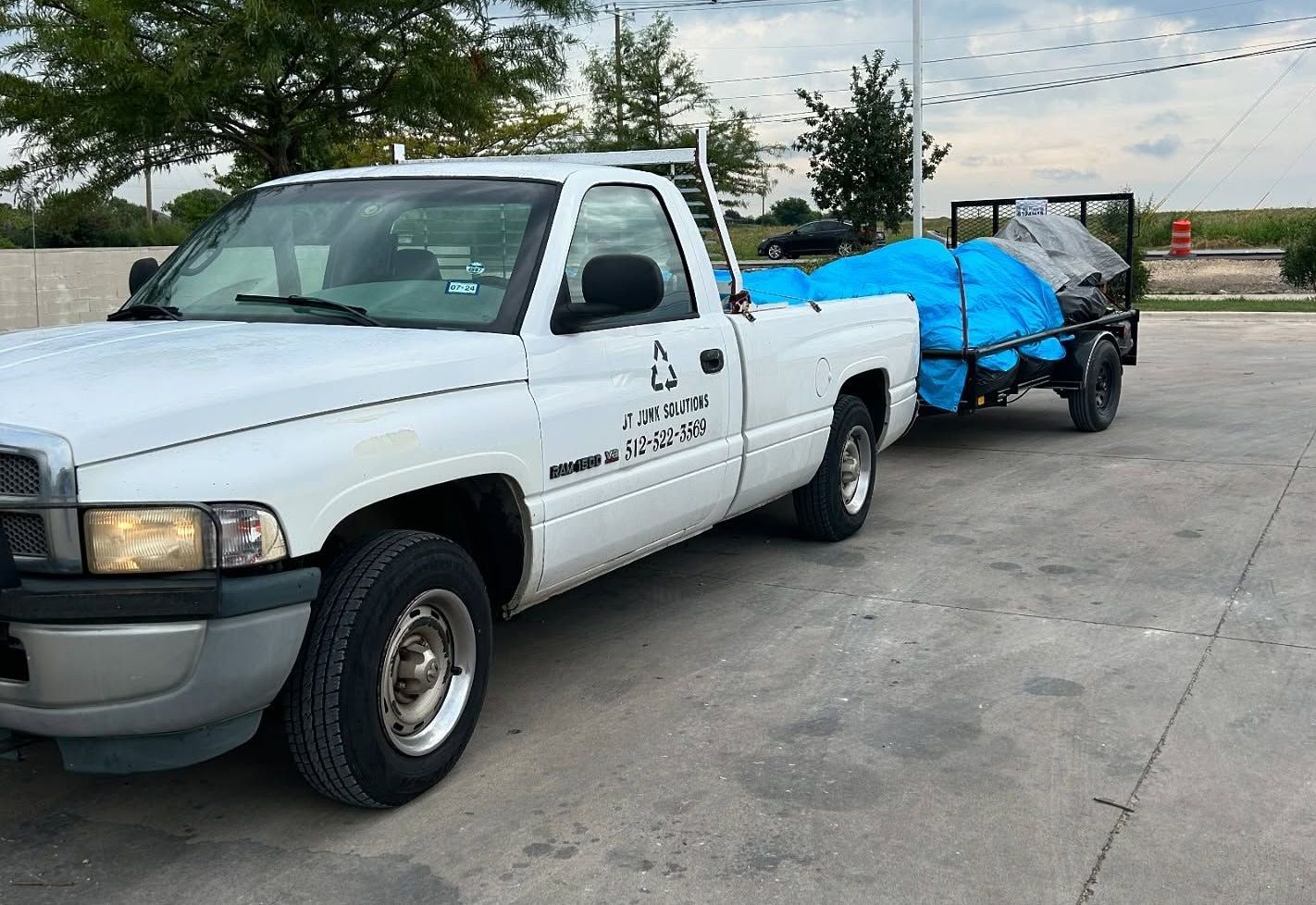 A white truck with a blue tarp on the back is parked in a parking lot.