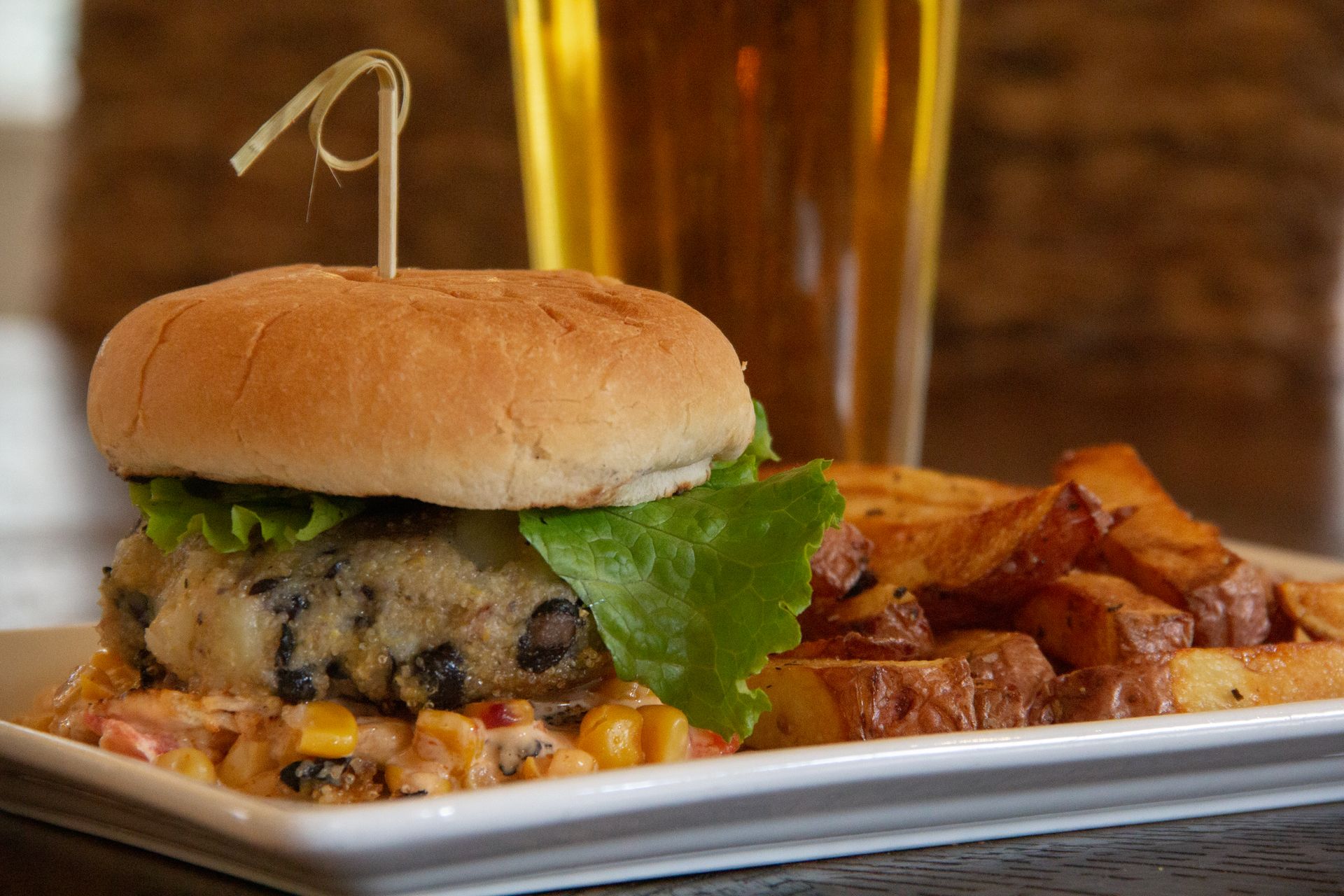 Burger with fries on a white plate, with a glass of beer in the background.