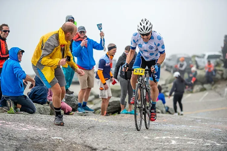 cyclist in a bike race pedaling up a rock face with people cheering him on