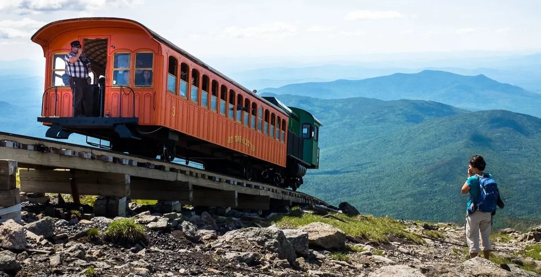 conductor on a mountain  train waving to a hiker with mountains in the background