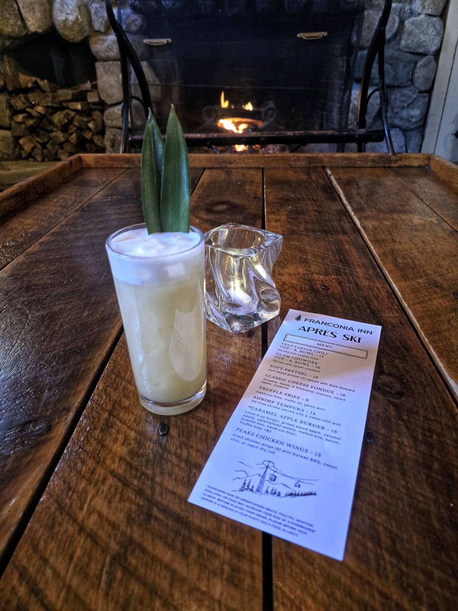 A cocktail on a wooden table in front of a fireplace