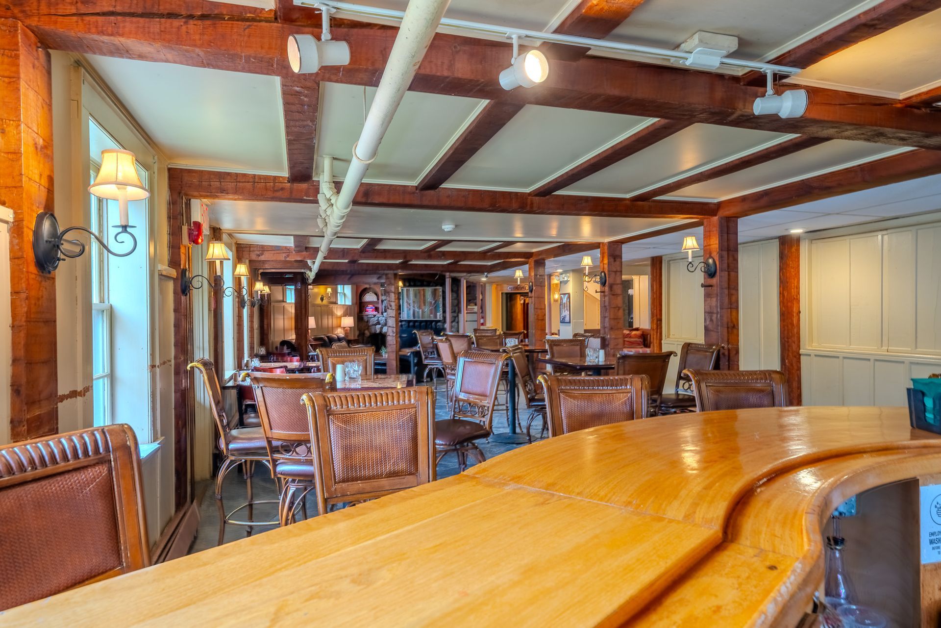 Wooden bar with interior of a restaurant, featuring tables and chairs, dark wood beams, and warm lighting.