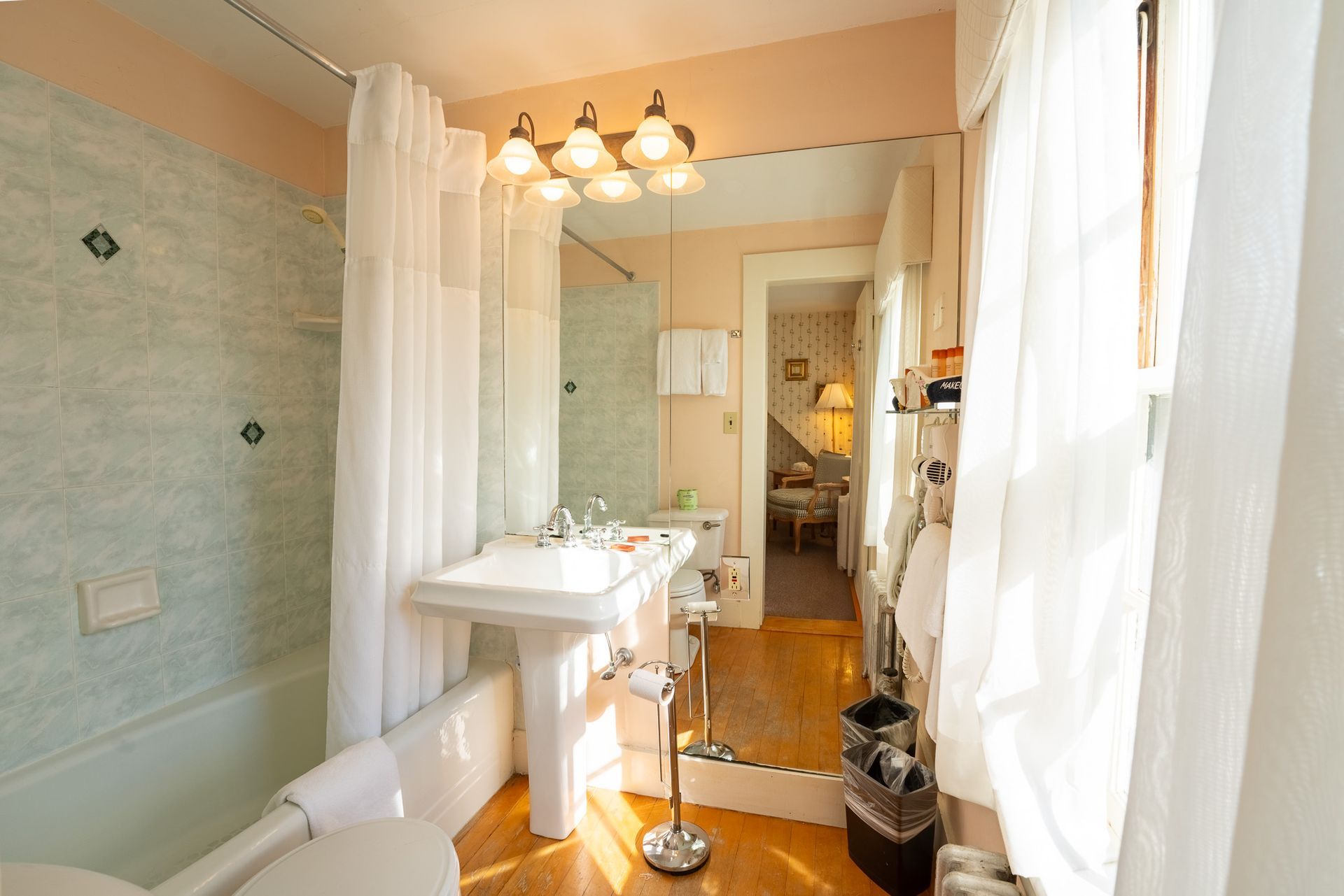 Bathroom with white pedestal sink, tub, and long mirror reflecting doorway to a room.
