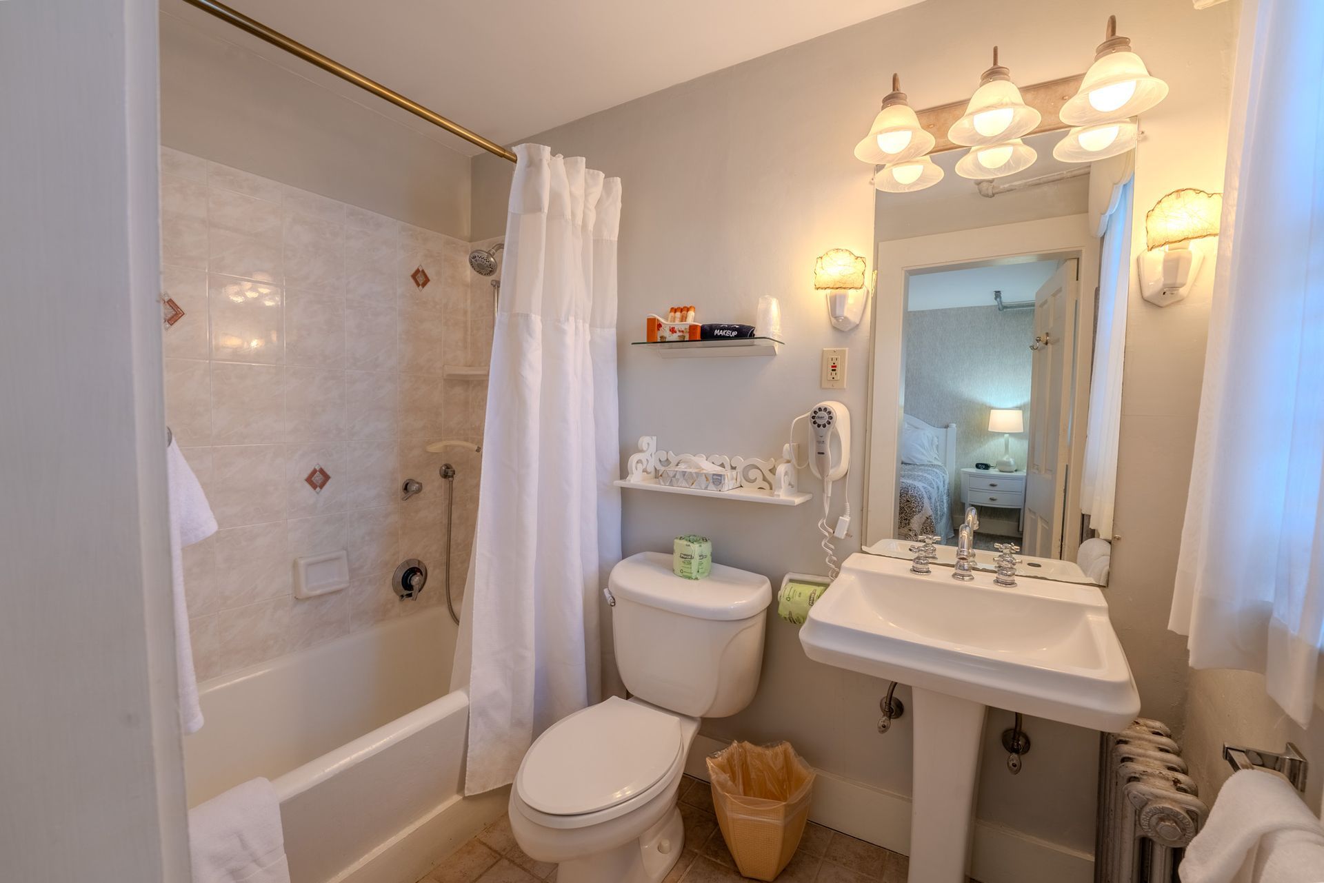 Bathroom with white tub/shower, toilet, pedestal sink, and mirror; window on right.