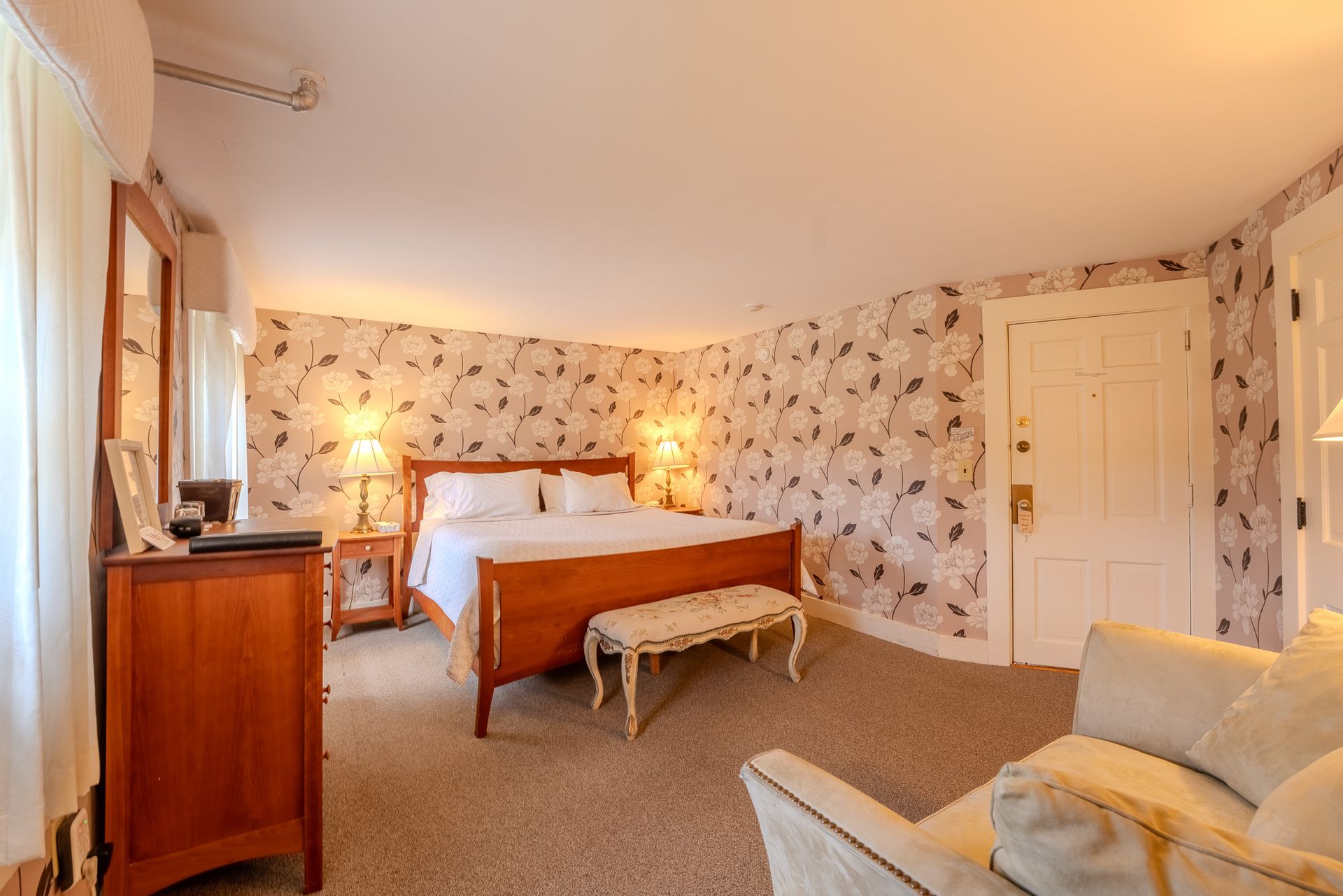 Bedroom with bed, floral wallpaper, dresser, and armchair.