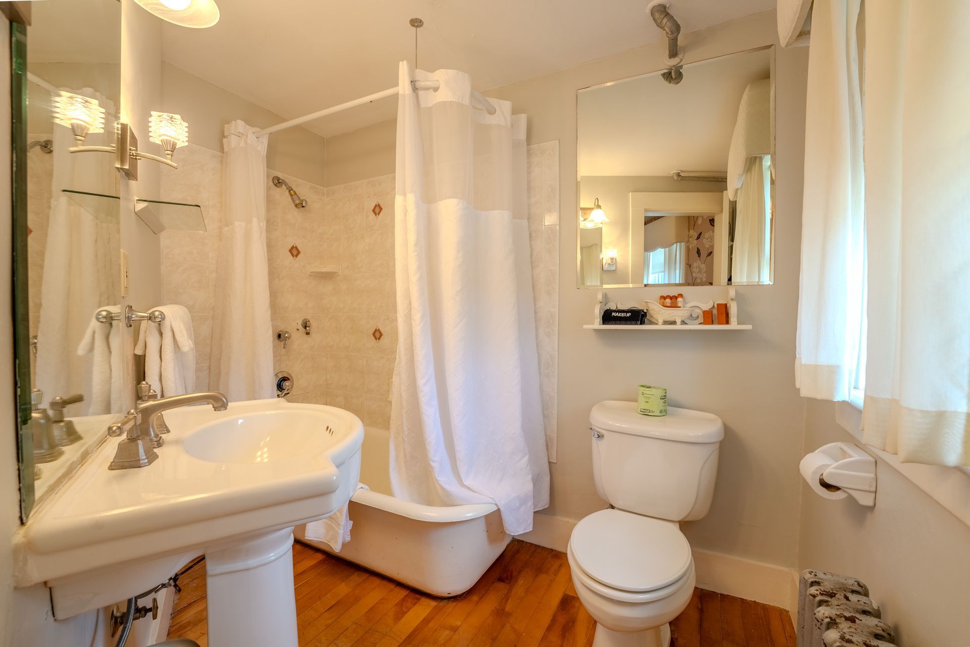 Bathroom with a pedestal sink, toilet, tub, and mirror. White and gold tones.