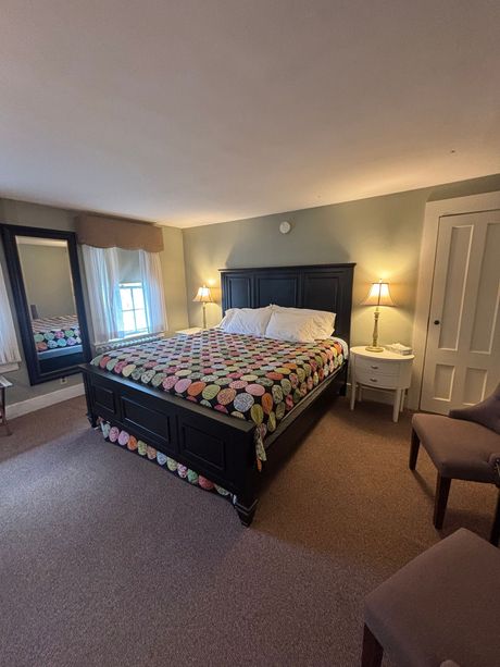 Bedroom with a large black bed, floral quilt, white nightstands, and a large mirror. Brown carpet and pale green walls.