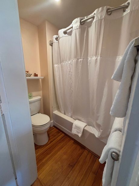 Bathroom with white shower curtain, toilet, towels, and wooden floor.