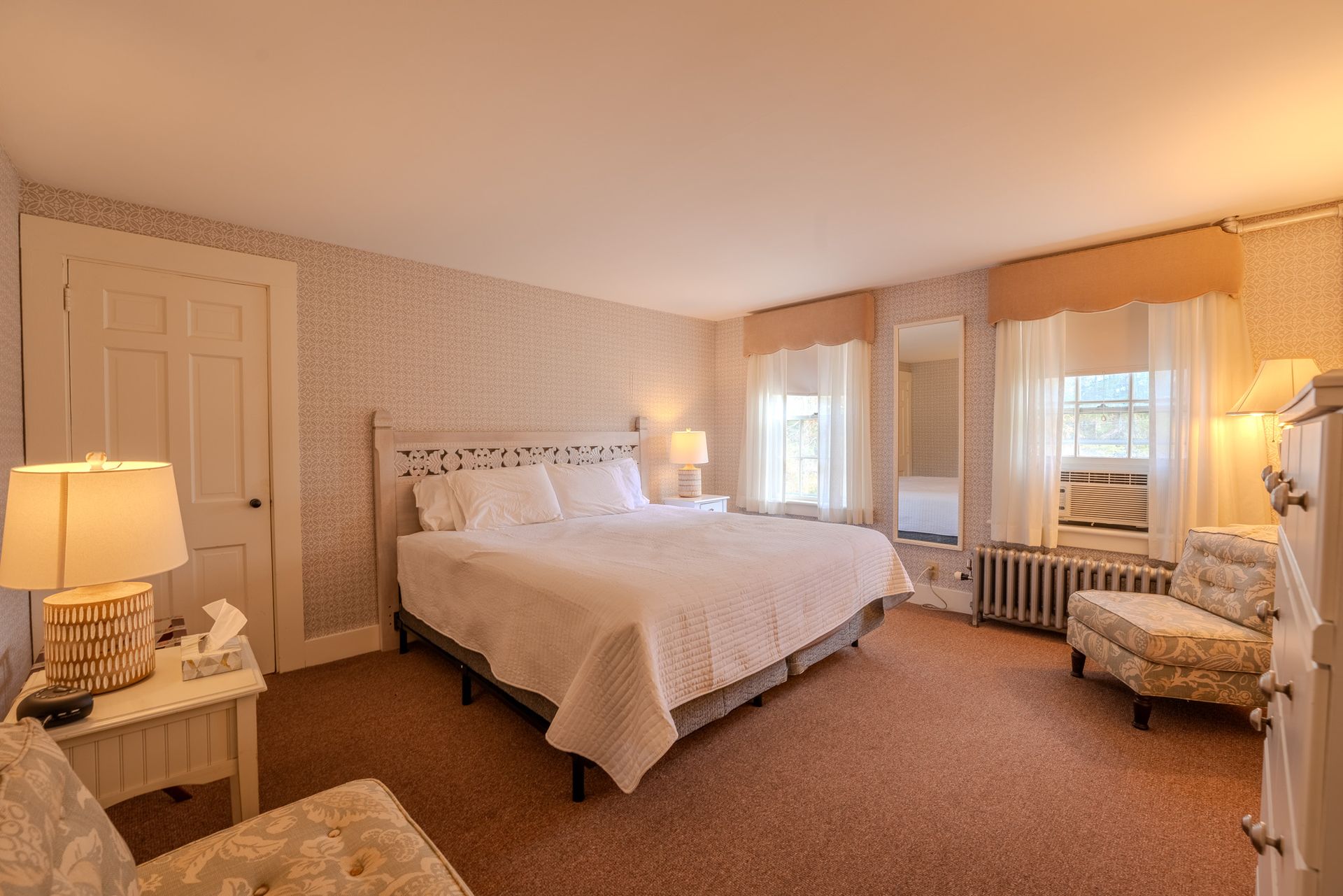 Bedroom with a king-sized bed, floral wallpaper, two windows, a chair, and a dresser.