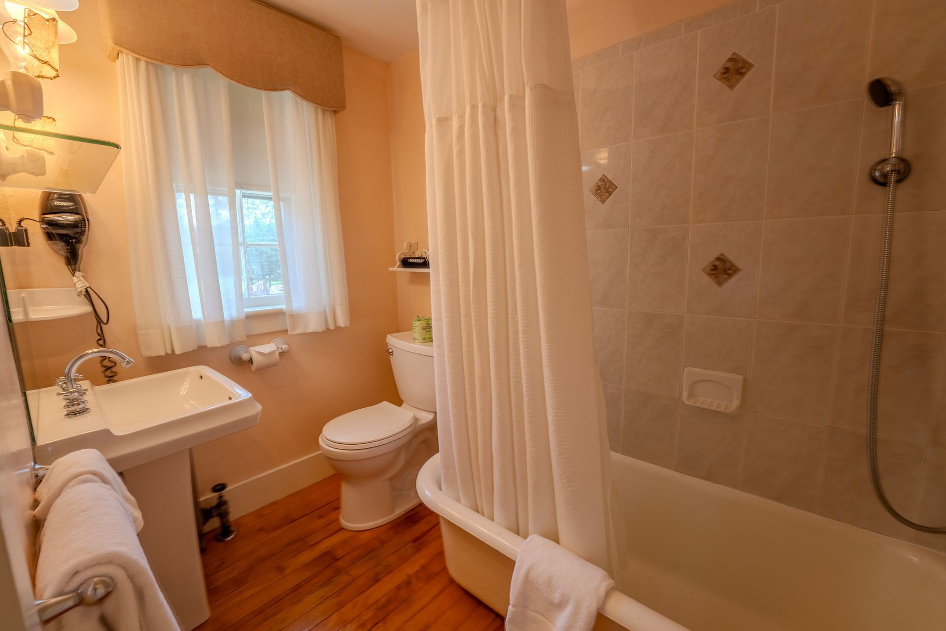 Bathroom with a white bathtub, toilet, and sink; the walls are peach colored and the floor is wood.