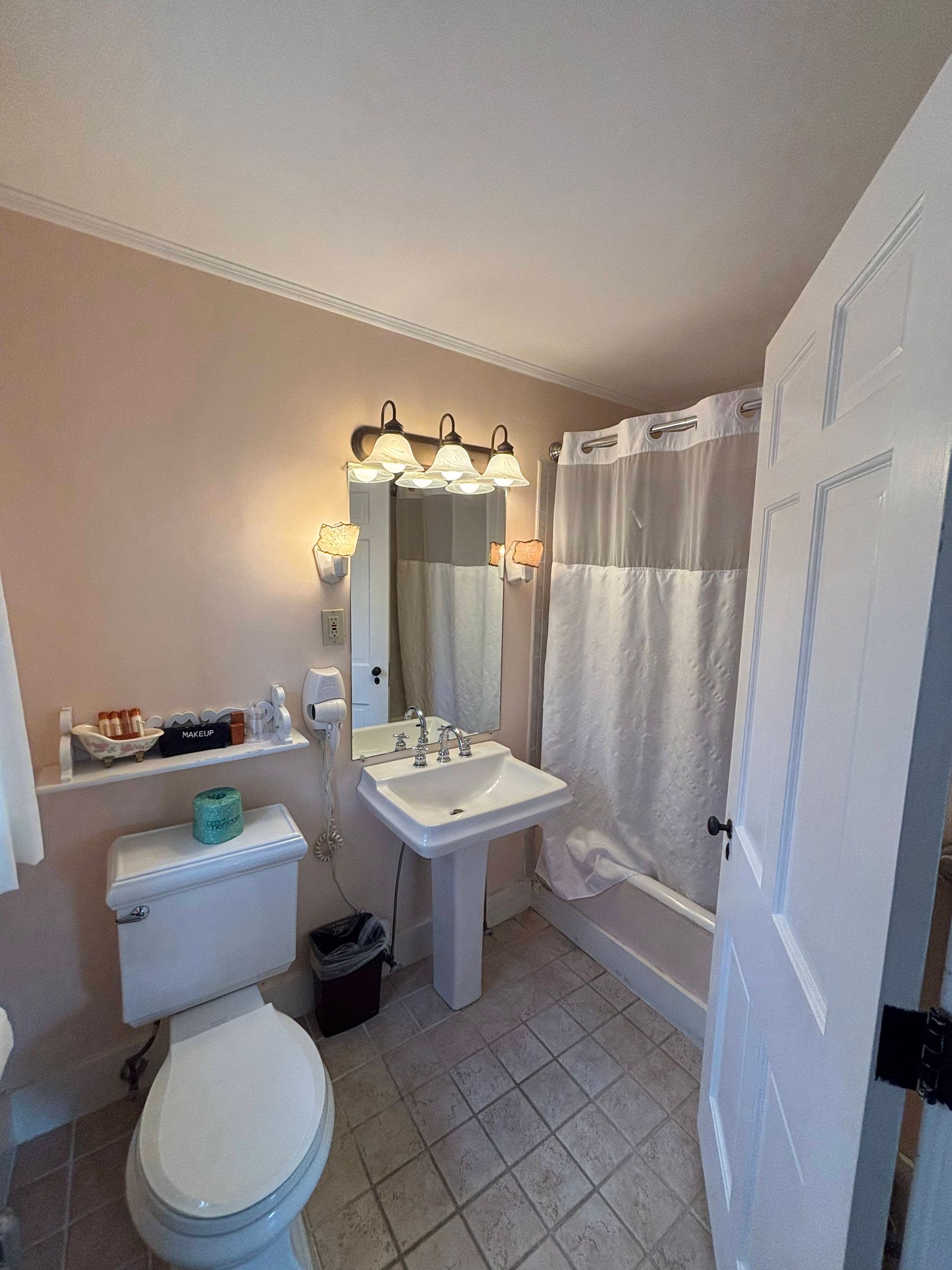 Bathroom with toilet, sink, bathtub, and white door; blush walls and gray floor tiles.