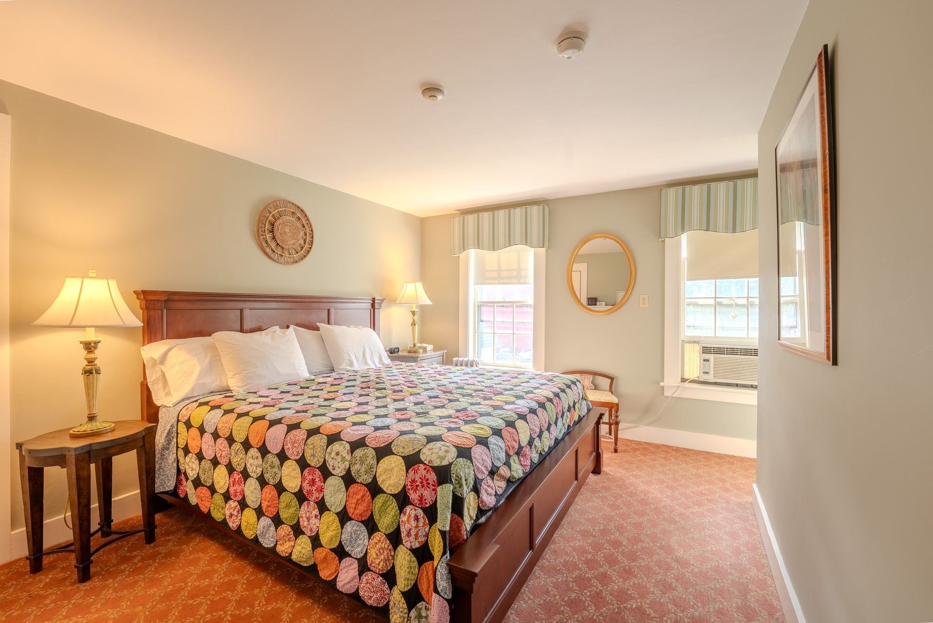 Bedroom with king-size bed, green walls, and a colorful quilt. Includes windows, side tables, and a mirror.