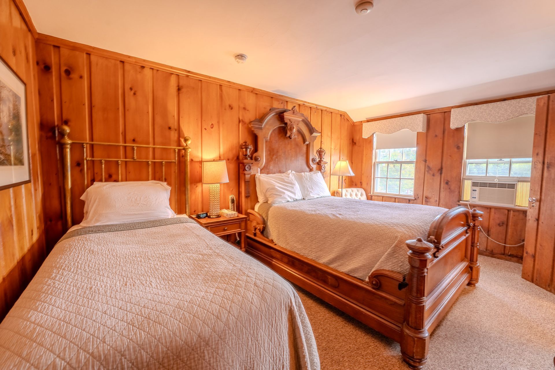 Bedroom with wood-paneled walls, two beds with white bedding, and two windows with shades.