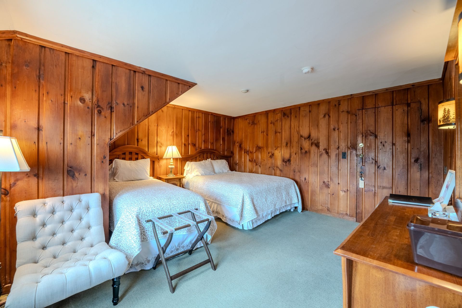 Bedroom with two twin beds, wood-paneled walls, a white chair, and a wooden dresser.