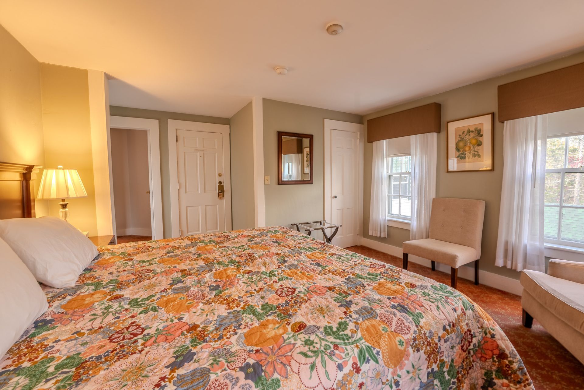 Bedroom with a floral bedspread, two windows with brown valances, and a tan chair.