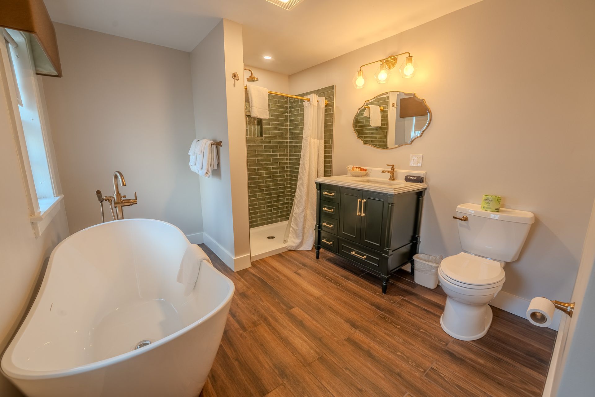 Bathroom with freestanding tub, dark vanity, shower, and wood-look floor.